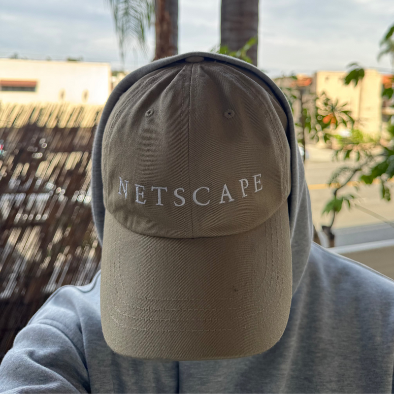 Person wearing a beige cap with 'Netscape' text, outdoors with palm trees and buildings in the background.
