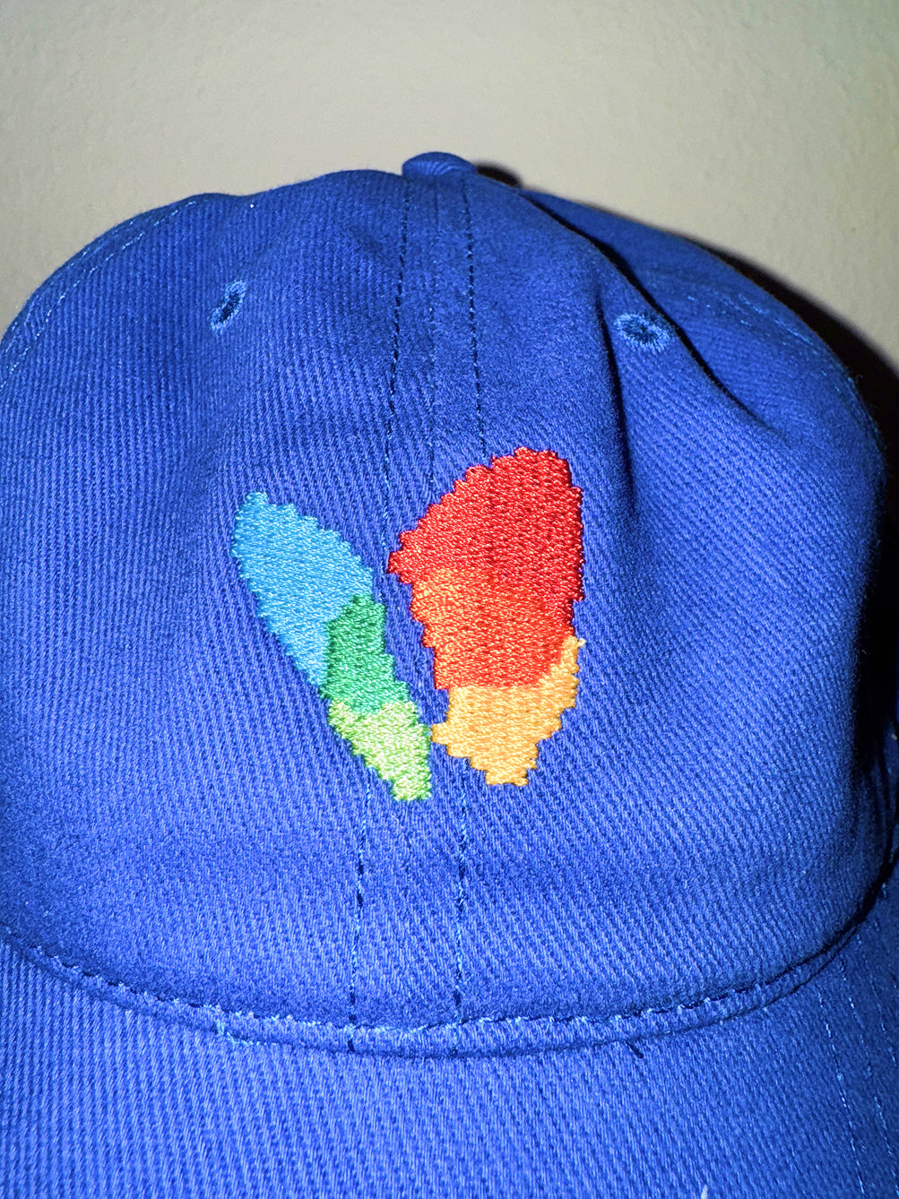 Close up of embroidered msn explorer icon on blue dad hat held by a hand against a neutral background in y2k flash photo style