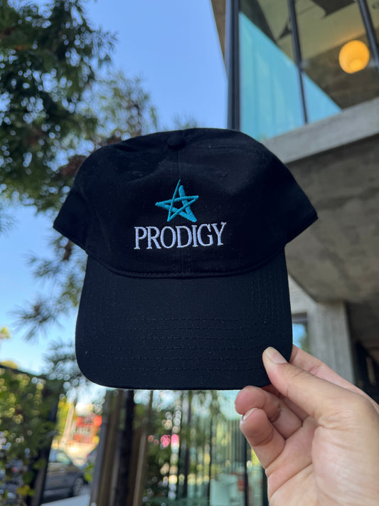 Black cap with 'Prodigy' logo held in front of a blurred outdoor background